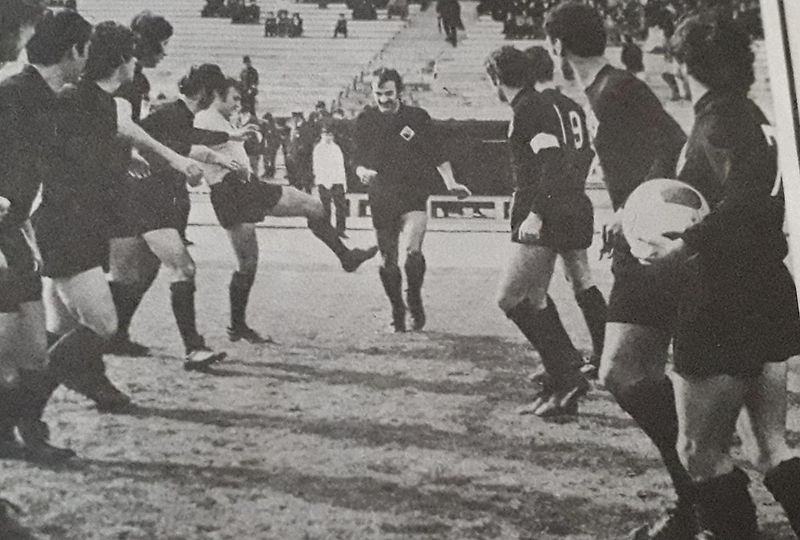 Black and white match photo of Académica players in black shirts on a worn pitch, one of them kicking the ball