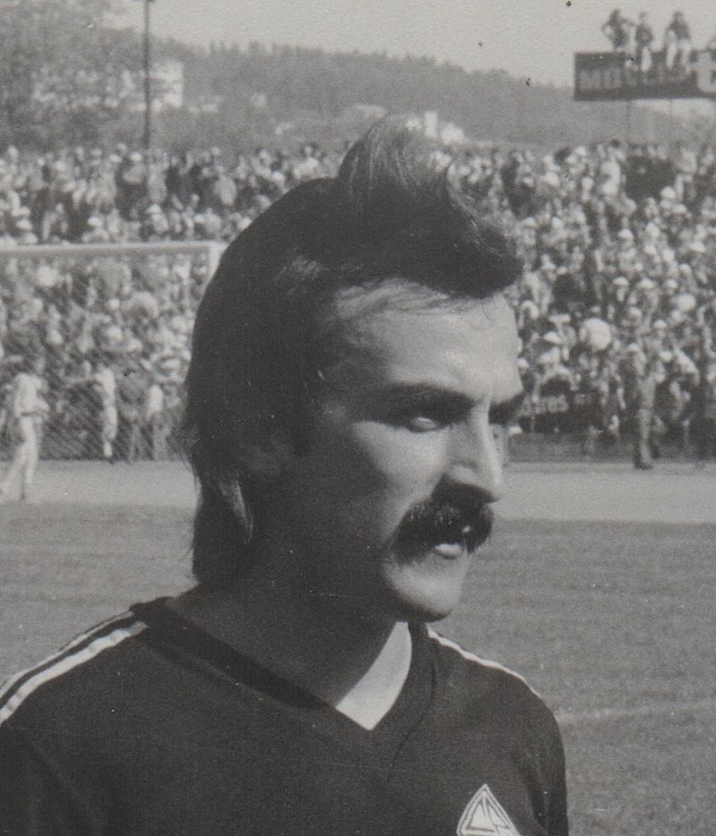 Black and white profile portrait of José Costa in the black Académica shirt, with a full stand behind him