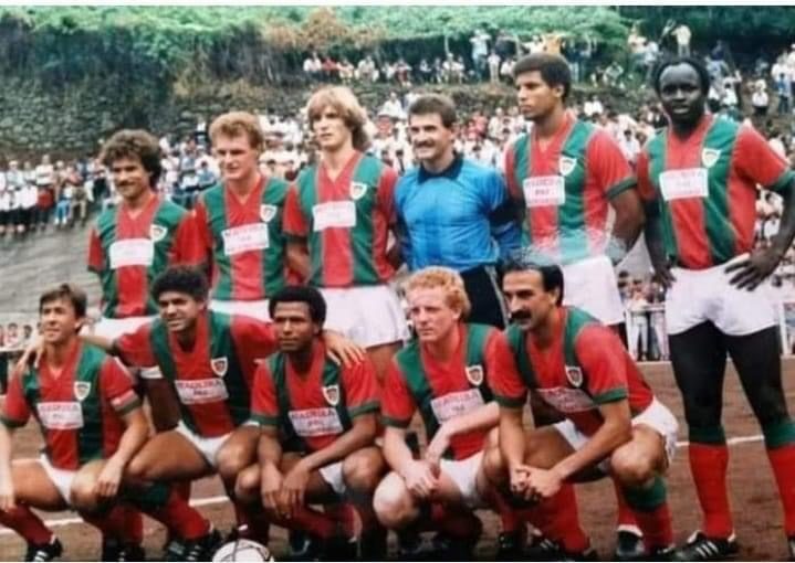 Marítimo team photo in red and green shirts, with fans on a hillside behind