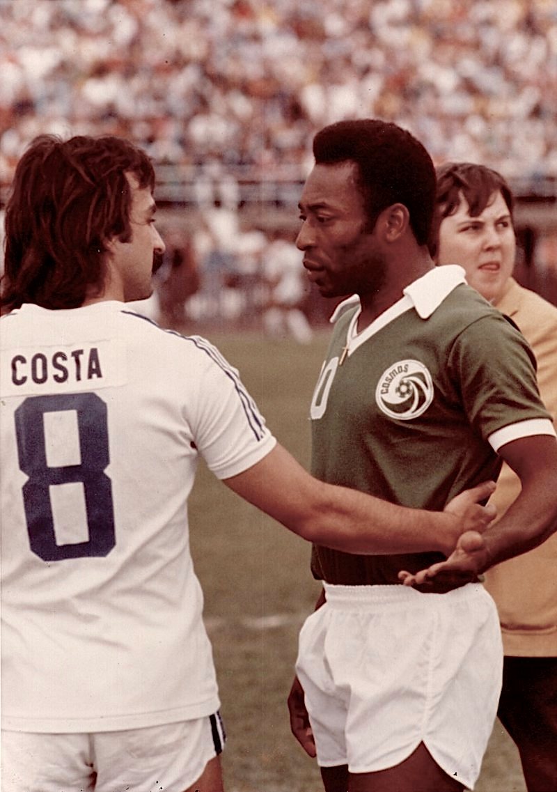 José Costa seen from behind in the white Rochester Lancers shirt with COSTA and No. 8 on the back, facing Pelé in the green New York Cosmos No. 10 shirt