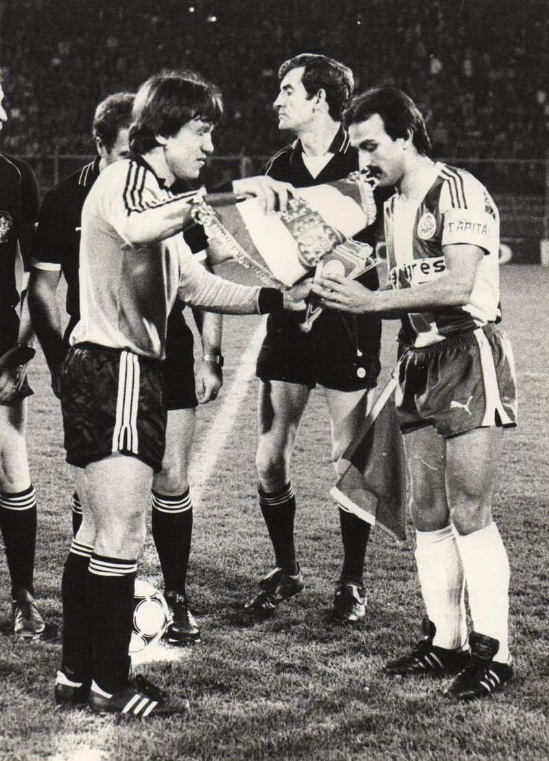 Black and white photo of two captains swapping pennants before a night game, with a referee between them